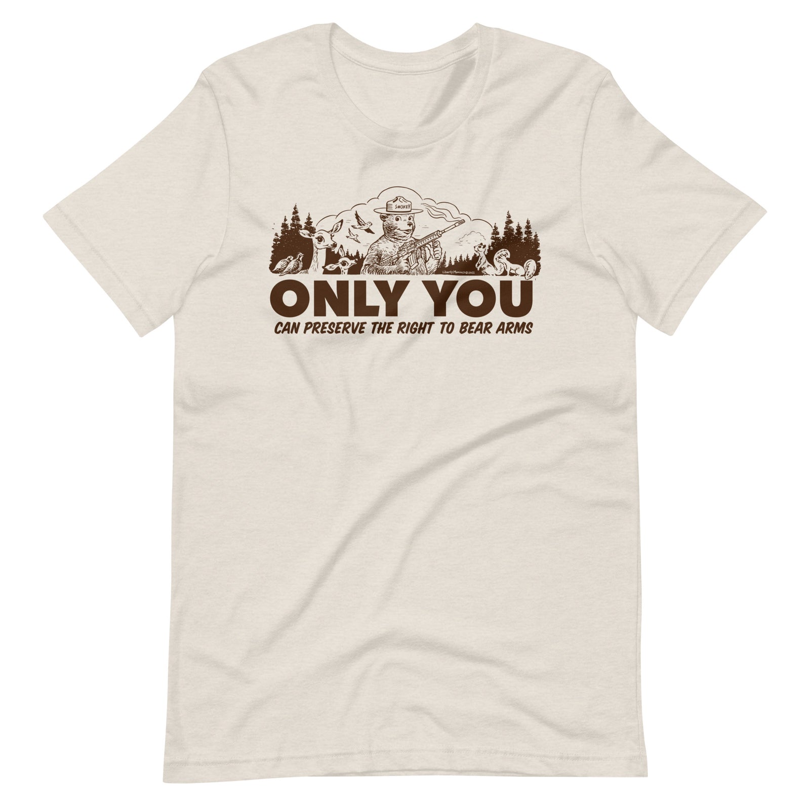 
A natural white t-shirt with a brown graphic. The graphic shows a cartoon bear resembling Smokey Bear, wearing a ranger hat and holding a hunting rifle. The bear is centered in a forest setting with a deer, squirrels, and birds nearby. Below the image, large text reads, "ONLY YOU CAN PRESERVE THE RIGHT TO BEAR ARMS."